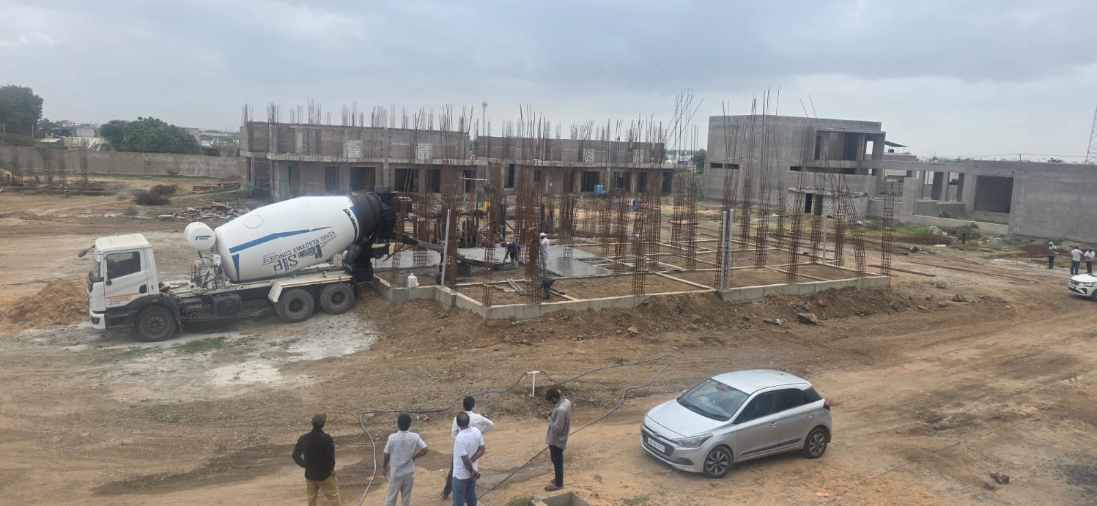 Transit mixer placing concrete beside reinforcement cages and a building frame
